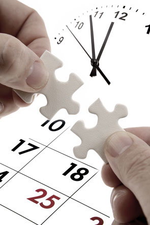 Hände, die zwei passende Puzzleteile vor einer Uhr und einem Kalender halten.